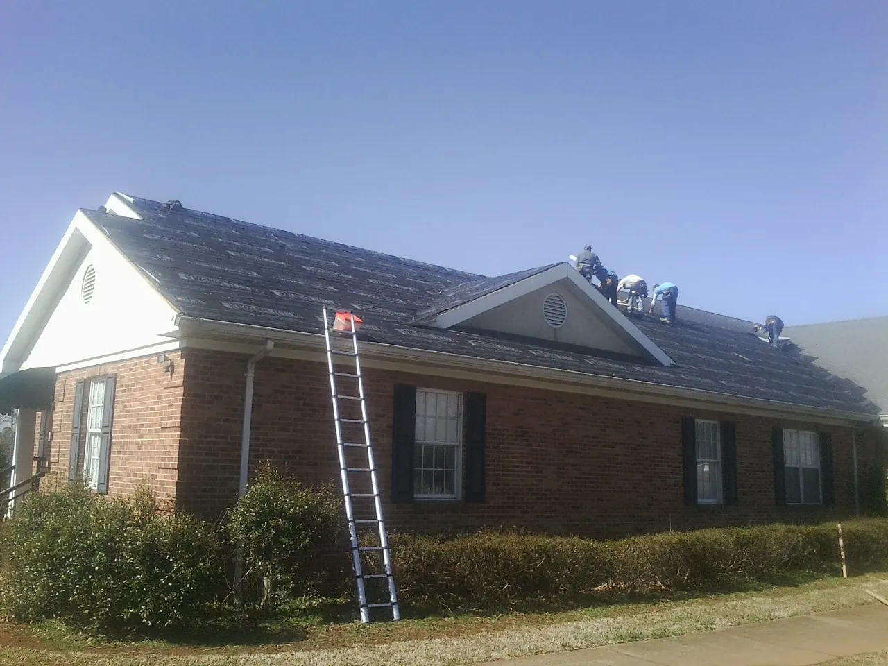 Crew tearing shingles off a brick ranch roof with a ladder set — Metal Roof Repair work by our crew in West Hills