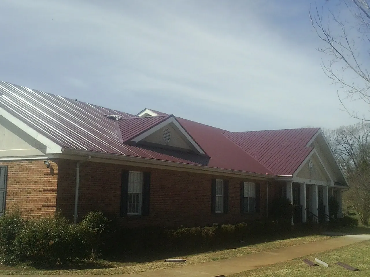 Red metal roof with gabled entries on a long brick building, from a Hail Damage Roof Repair job in West Hills