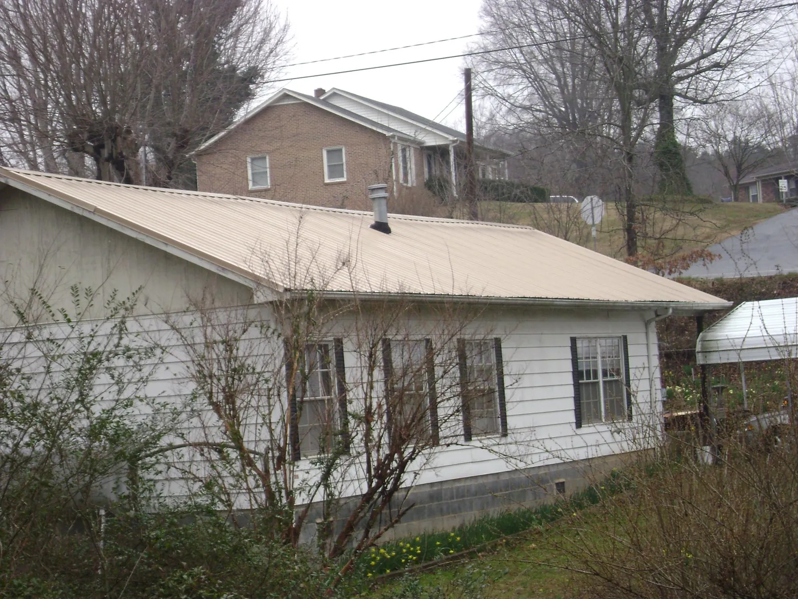 Tan metal roof on a white sided house set into a hillside — Commercial Roofing by Roofing Brothers in West Hills